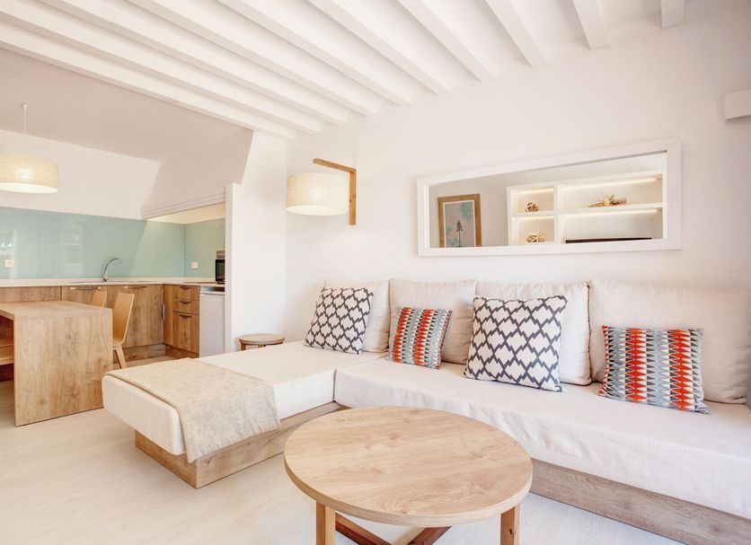 Grupotel Aldea Cala'n Bosch living area with sofa, wood table and open kitchen in Ciutadella de Menorca