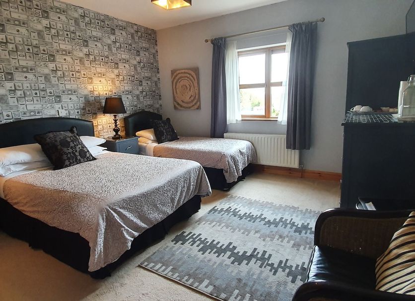 Church View B&B in Gorteen guest room with two beds, patterned rug, window, and armchair