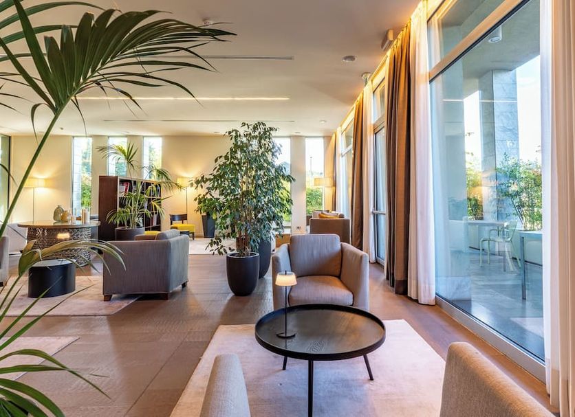 Hsm Hotel San Martino in Garbagnate Monastero lounge with armchairs, plants and floor-to-ceiling windows