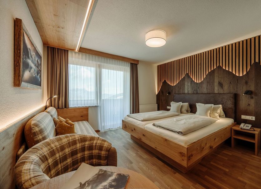 Hotel Waldfrieden in Rohrmoos guest room with wooden bed, sofa, and balcony doors