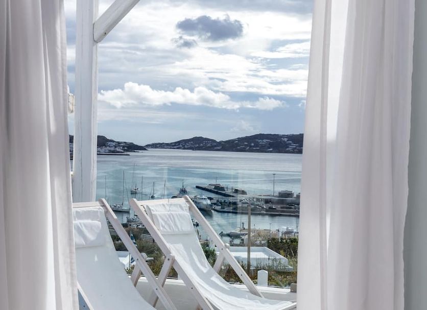 Rhenia Hotel in Tourlos with balcony sea view, lounge chairs, and harbor boats beyond glass railing