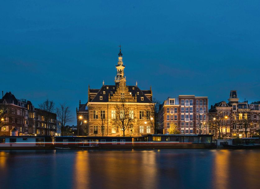 Pestana Amsterdam Riverside hotel on the canal in Amsterdam at dusk with illuminated historic buildings