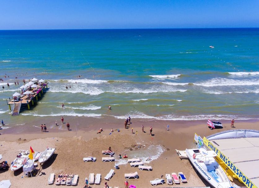 Side Village Hotel in Side overlooking a sandy beach with sun loungers, a pier, and turquoise sea