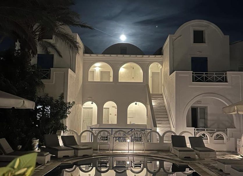 Night view of Pension George in Karterados with a lit pool courtyard and arched balconies