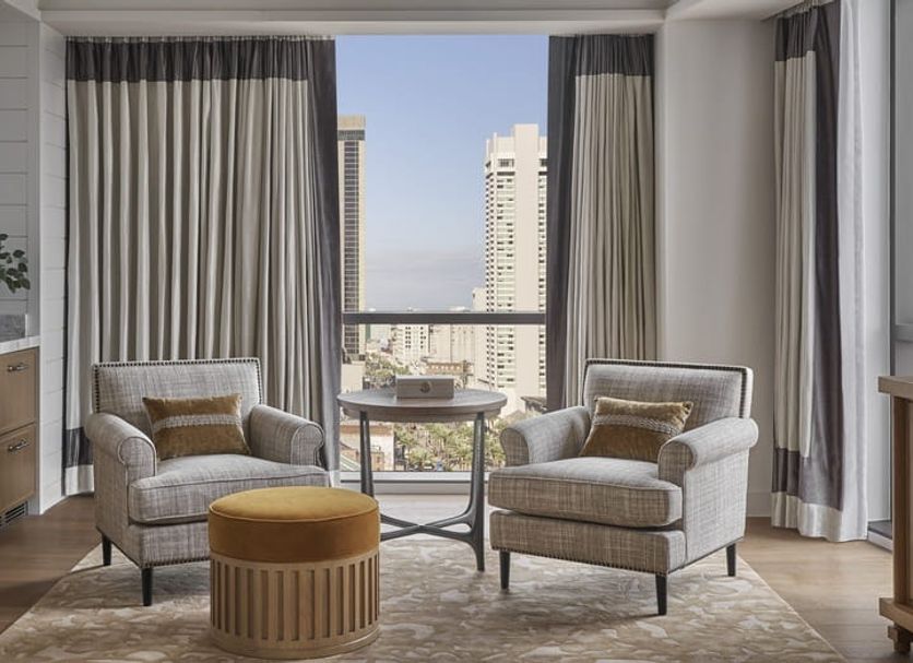 Four Seasons Hotel New Orleans suite with city skyline view, two armchairs, and a round table by tall windows
