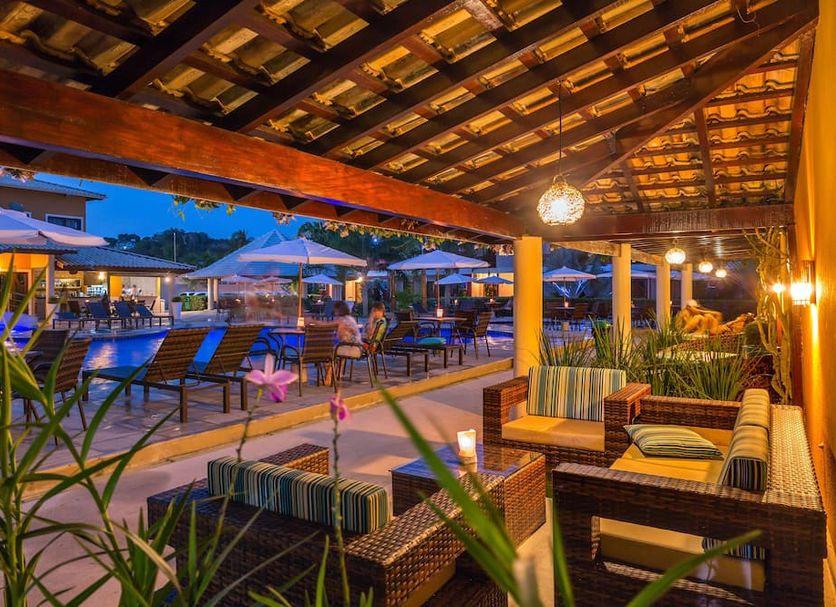 Vitoria Regia Praia Hotel in Porto Seguro: open-air poolside lounge with wicker seating at dusk