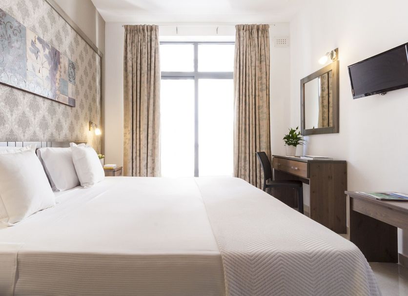 Alexandra Hotel in St. Julian's guest room with twin beds, wall-mounted TV, desk, and tall window