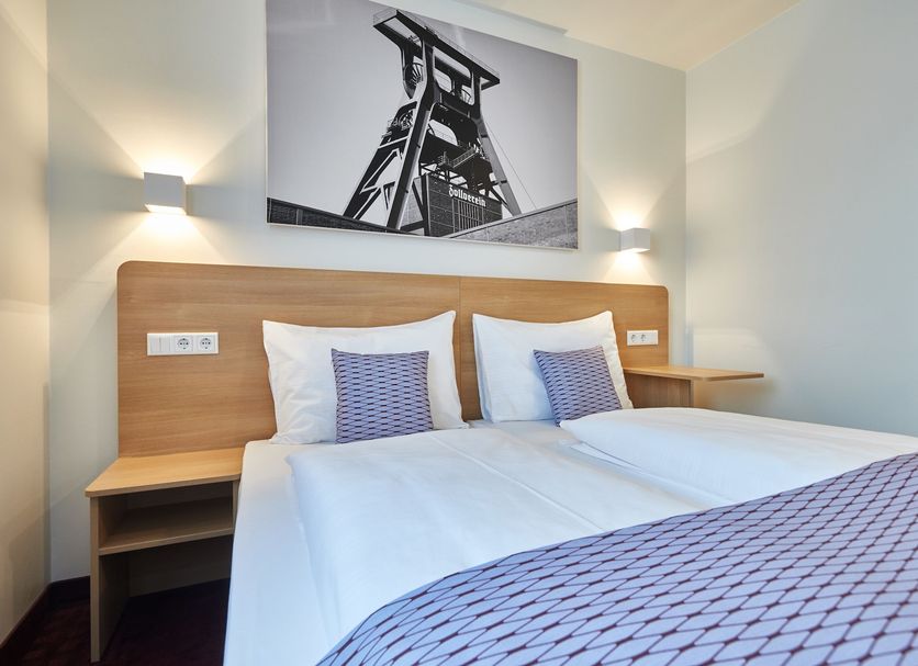 Mcdreams Hotel Essen room with twin bed, wood headboard, bedside shelves, and black-and-white wall art