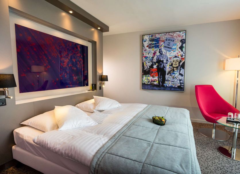 Starling Hotel Lausanne room in Saint-Sulpice with king bed, red chair, floor lamp and wall art