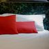 Hotel Napoleon Bastia bed with white linens and red accent pillows against a dark patterned headboard
