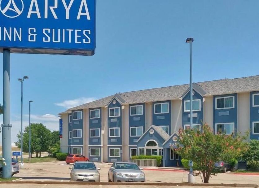 Arya Inn & Suites in Irving exterior with sign, parking lot, and three-story hotel building
