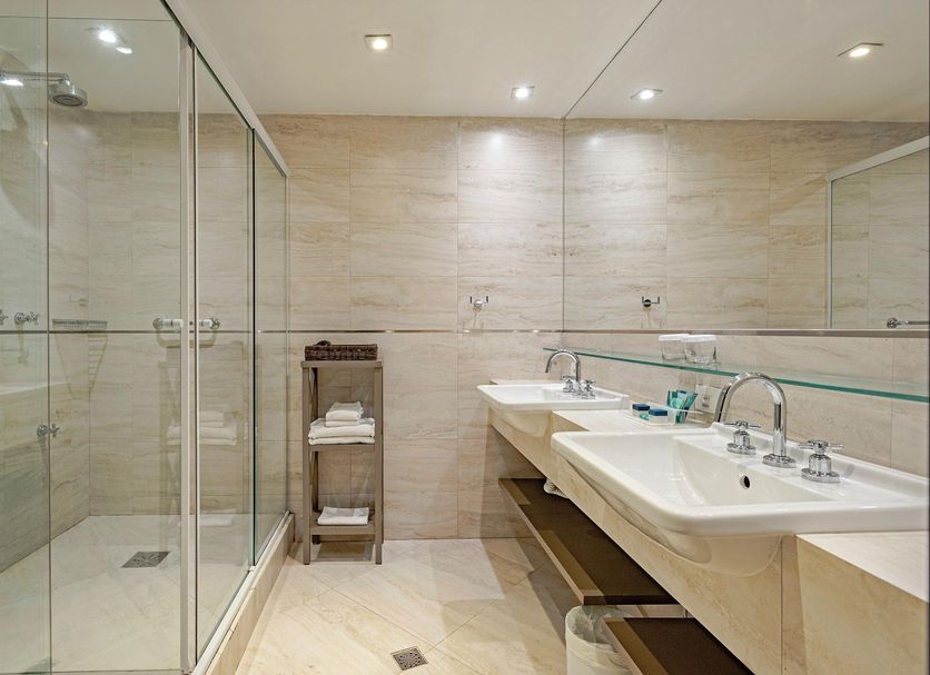 Slaviero Baia Norte Florianópolis bathroom with glass shower, double sink vanity and beige tile