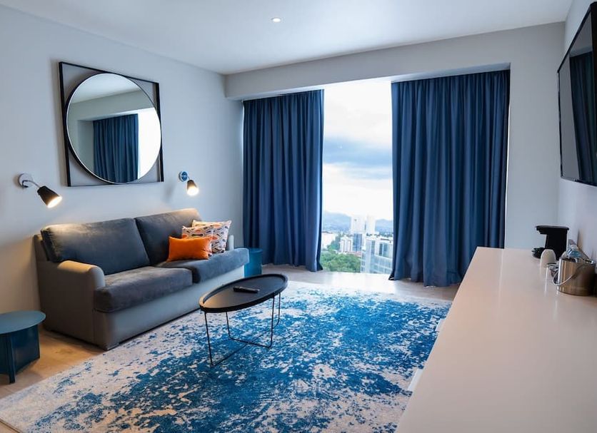 Hilton Garden Inn Mexico Santa Fe room with sofa, city view, blue curtains and patterned rug in Mexico City