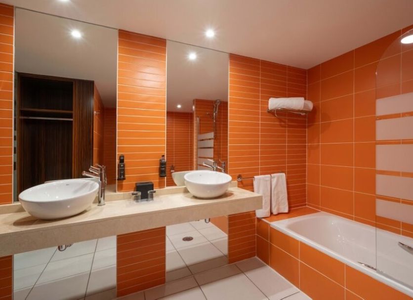 Exe Convention Plaza Madrid bathroom with orange tile walls, double sinks, mirror, and bathtub in Madrid