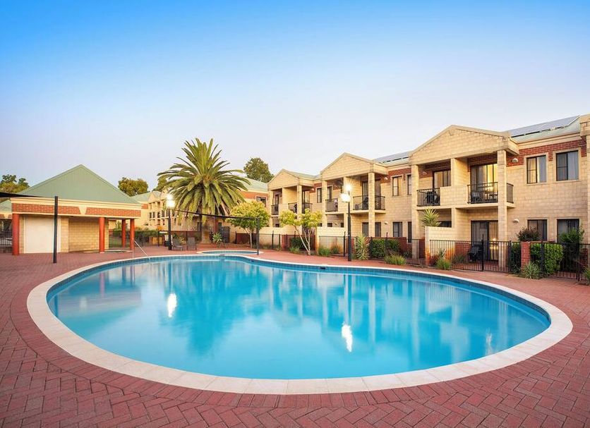 Country Comfort Perth in Belmont: outdoor pool with palm tree and two-story hotel buildings