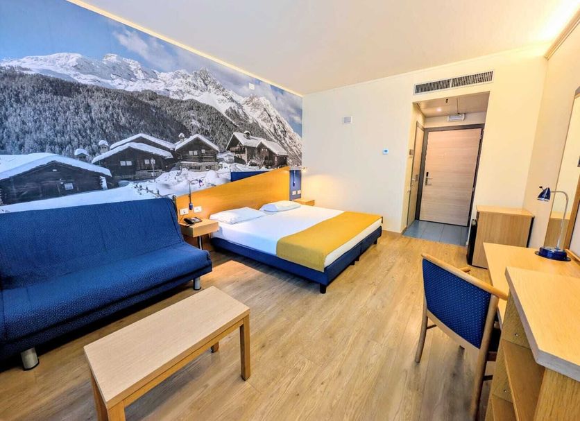 Hotel Express Aosta East in Pollein: room with bed, sofa, desk and mountain mural