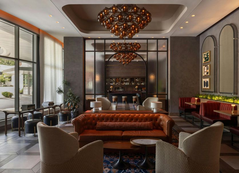 The Tess, Autograph Collection Atlanta lobby lounge with chandeliers, leather sofa, and bar seating
