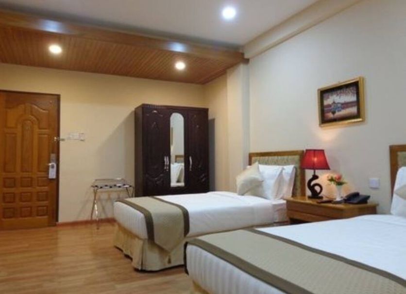 Royal Khattar Hotel Yangon guest room with two beds, wardrobe, bedside lamp, and wood-paneled ceiling