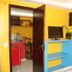 Pousada Innova in Natal guest room with TV, blue shelving, open door to kitchenette, and yellow walls