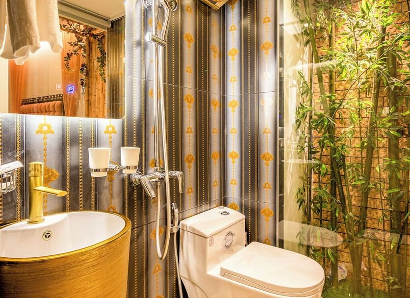 Mai Hotel Hanoi bathroom with gold sink, toilet, shower and bamboo garden-style wall