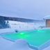 Landhotel Moorhof in Neuschönau: snowy outdoor pool glowing green beside the hotel at dusk
