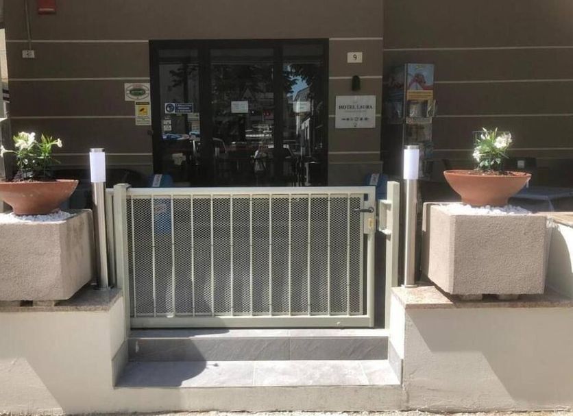 Hotel Laura, Rimini: hotel entrance with metal gate, glass doors, and potted plants on stone pedestals