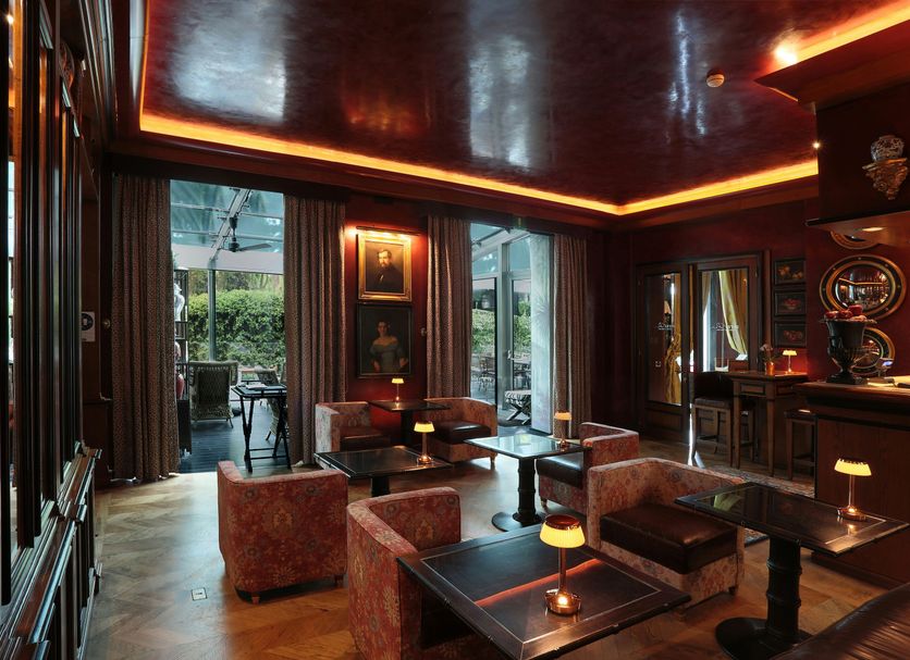 Hotel de la Ville Monza lounge with dark wood paneling, bar seating, and open doors to the terrace