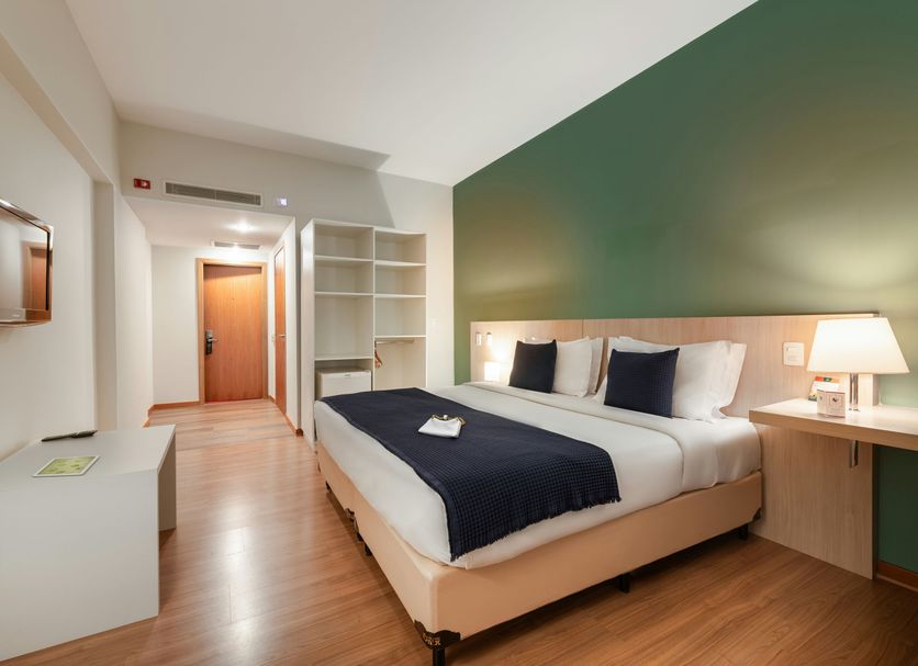 Pestana Curitiba guest room with double bed, wood floors, desk, shelves and green accent wall