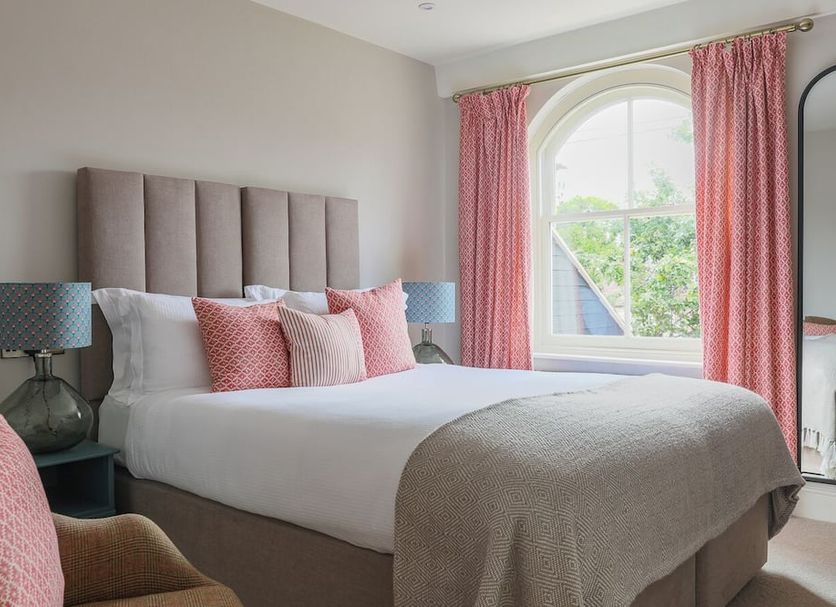 The Bear Hotel, Wareham bedroom with pink curtains, upholstered bed, and arched window view