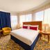 City Seasons Al Hamra Hotel in Abu Dhabi guest room with king bed, curved windows and colorful carpet