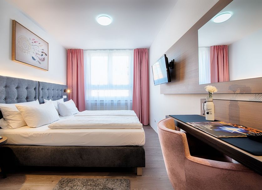 Home Hotel Dortmund guest room with double bed, desk, wall-mounted TV and window with pink curtains