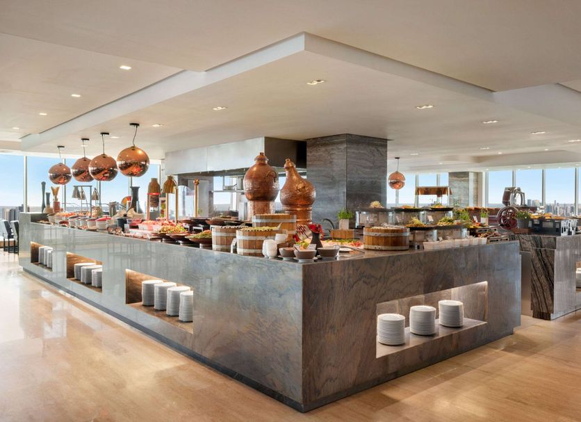 Wyndham Grand Manama buffet dining area with copper pendant lights and city views