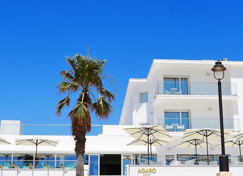 Hotel Agaró in Chipiona with white facade, palm tree, and terrace umbrellas under a blue sky