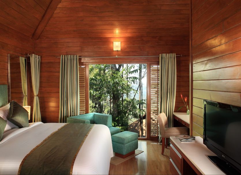 The Tamara Coorg Madikeri bedroom with king bed, TV, and balcony view of lush greenery