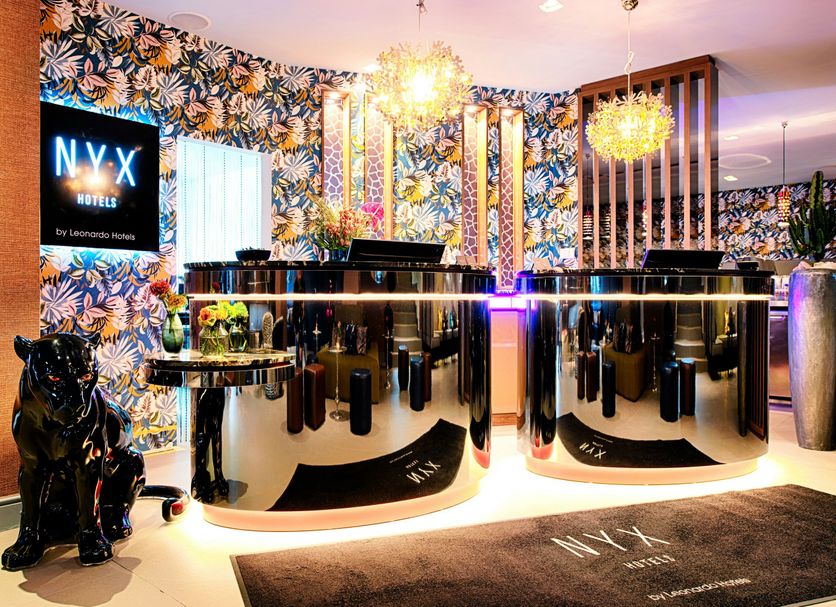 NYX Hotel Mannheim by Leonardo Hotels lobby with floral wallpaper, glossy reception desks and chandeliers