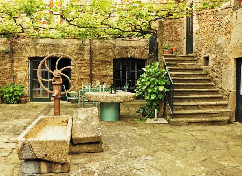 San Nicolas in Santiago de Compostela: stone courtyard with vine-covered pergola, bench, table, and stairway