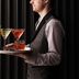 Hyatt Regency London Stratford server carrying cocktails on a tray against dark curtains
