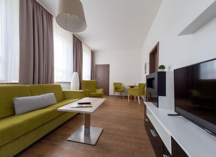 Hotel am Stadtpark Nordhausen living room with green sofa, TV, and dining area