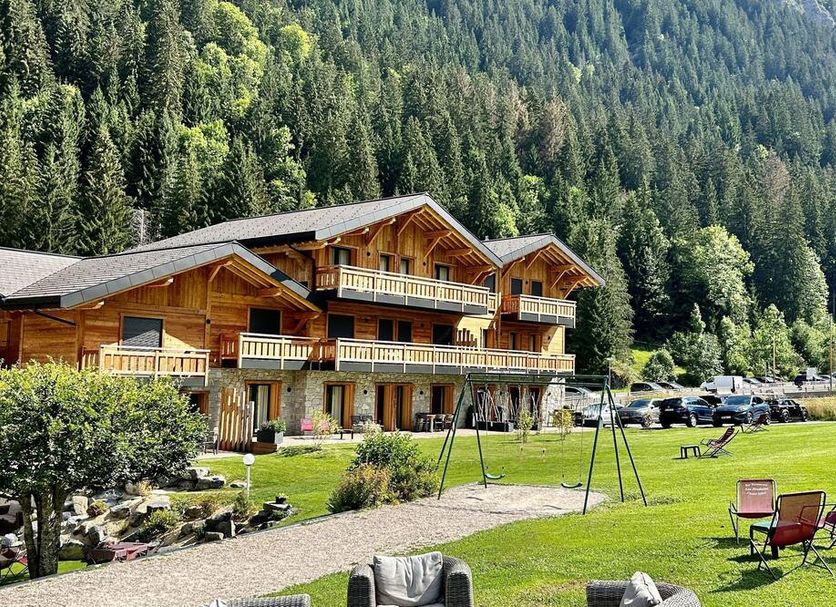 Hameau des Prodains - Hôtel in Morzine with alpine lodge exterior, lawn, and mountain forest backdrop