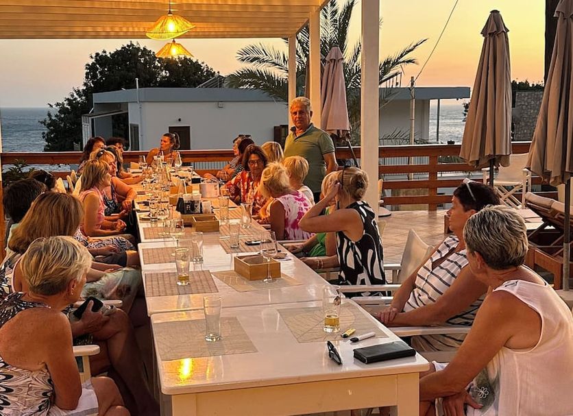 Mary Popi in Panormos: outdoor terrace dining at sunset with sea view and guests at a long table