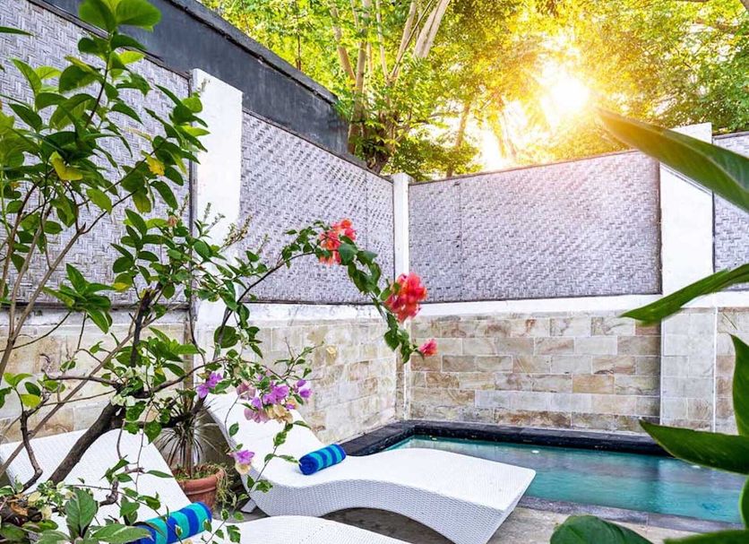 Tír na nÓg Beachfront Resort in Mataram with a small pool, lounge chairs and tropical garden at sunset