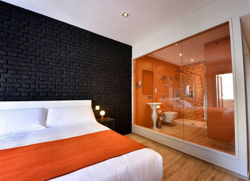 Quaint Boutique Hotel Sannat room with orange bedspread and glass-walled bathroom in Sannat