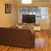 Westside Studio Apartments in Armidale living room with brown sofa, TV stand and large window blinds