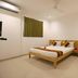Hotel De Ecobiz in Ahmedabad room with double bed, desk, chairs, and wall-mounted TV