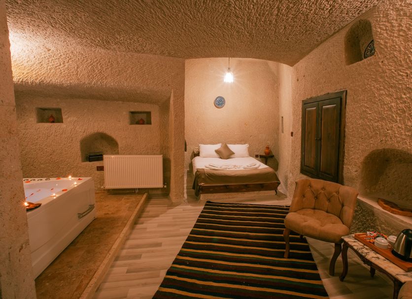 Mia Cappadocia Cave Hotel in Göreme cave room with striped rug, bed, sitting chair, and bathtub
