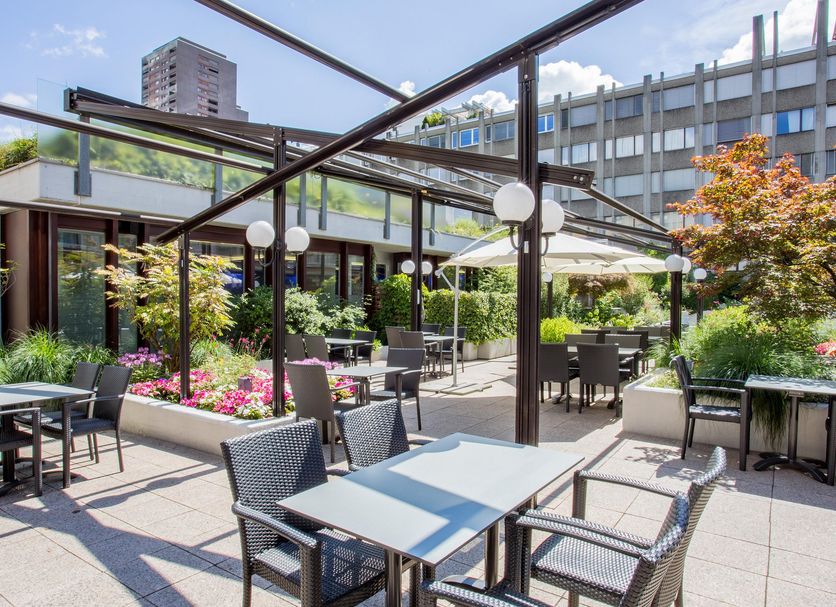 Crowne Plaza Zurich By IHG courtyard terrace with outdoor tables, greenery and city-view surroundings
