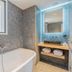Yuna Porte-Maillot aparthotel in Paris bathroom with freestanding tub, stone walls and lit vanity mirror