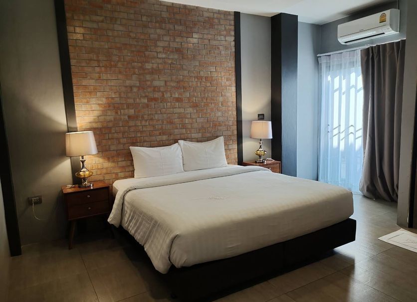 Qoo Hotel Buri Ram guest room with king bed, brick accent wall, bedside lamps and air conditioner