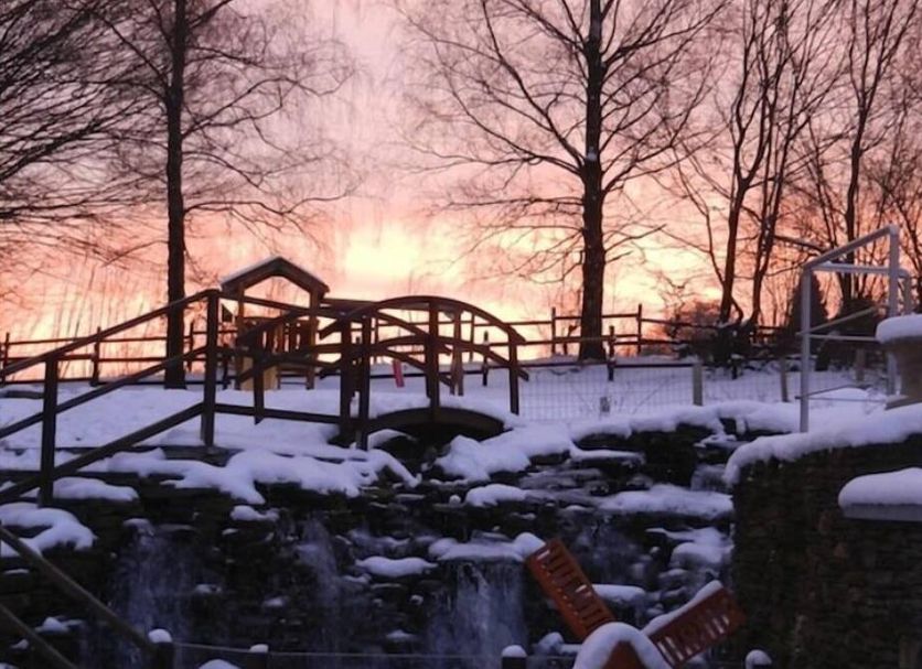 Le 'Ti 'Bou De Refuge in Bouillon with a snowy garden bridge and small waterfall at sunset