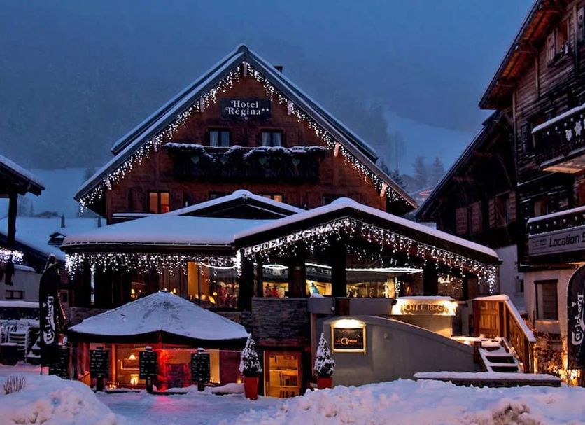 Chalet Hotel Régina in Les Gets, snow-covered alpine lodge lit up with festive string lights